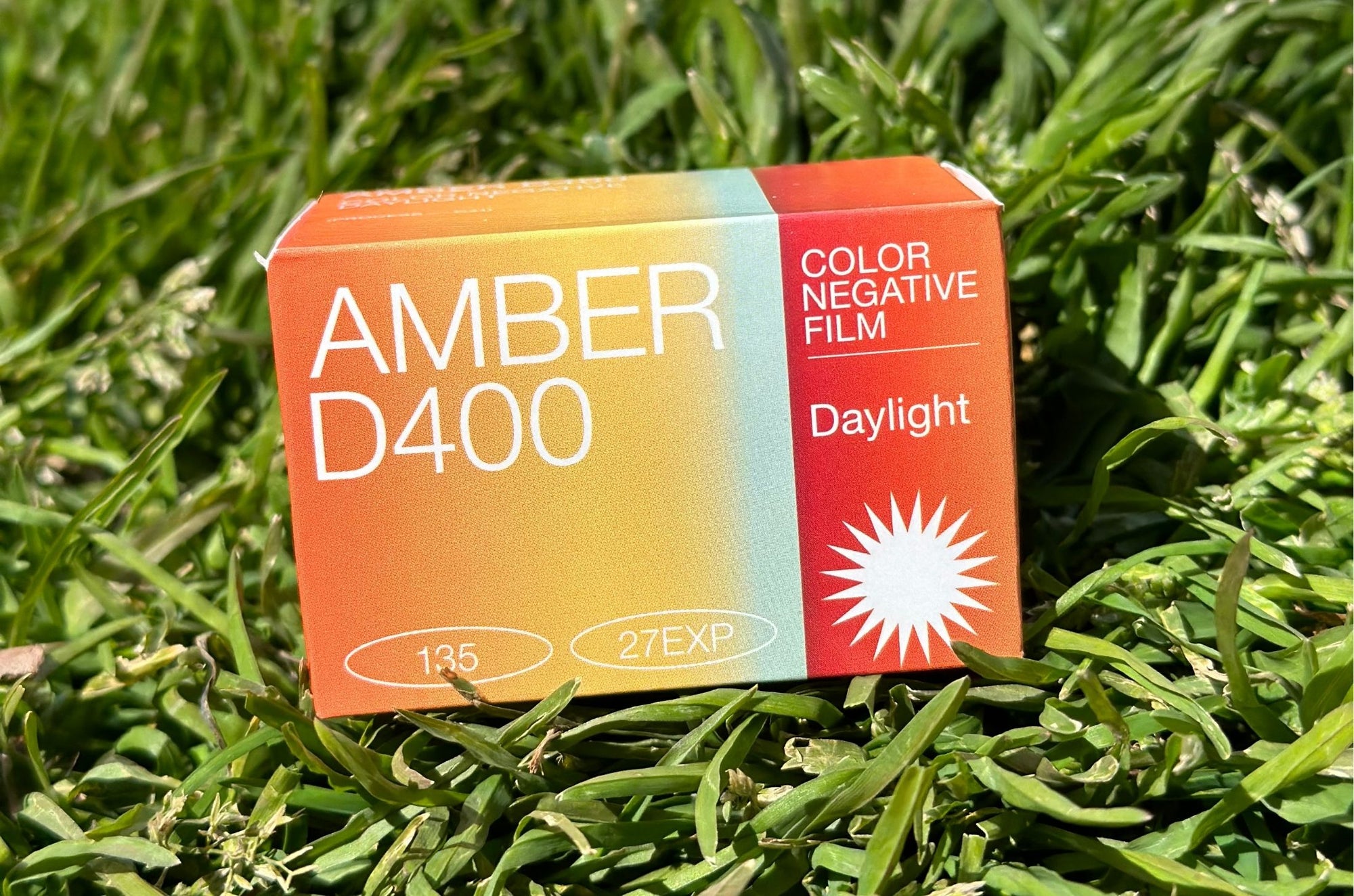 AMBER D400 color negative film box, 135 format, 27 exposures, designed for daylight use, resting on green grass.