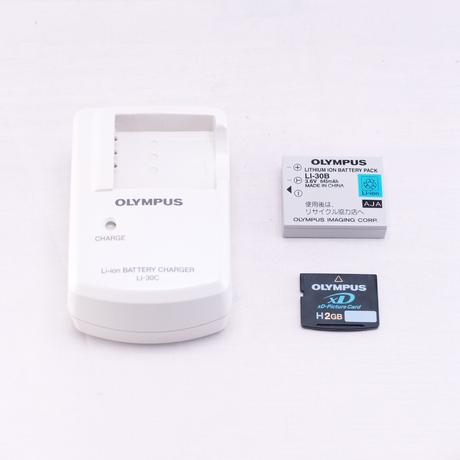 OLYMPUS battery charger with lithium-ion battery pack and 2GB memory card on a white background.