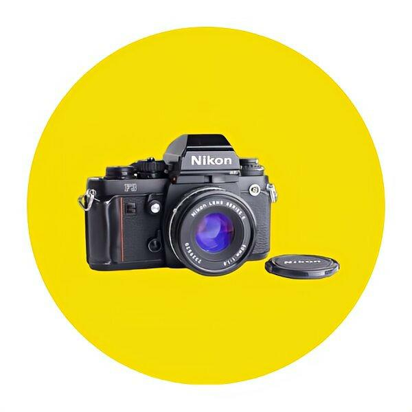 Nikon F3 35mm film camera with lens cap on a bright yellow background.