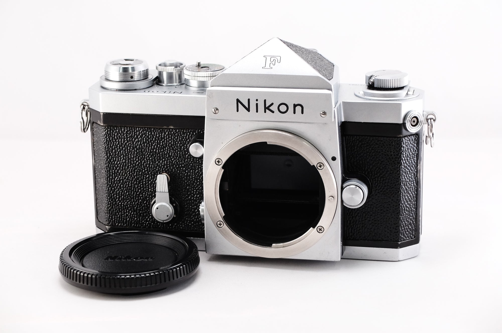 Nikon F film camera body with lens mount and cap, featuring a classic silver and black design.