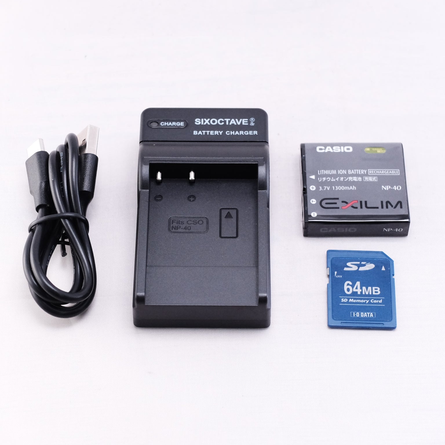 Casio battery charger with lithium-ion battery, USB charging cable, and 64MB SD memory card on a flat surface.