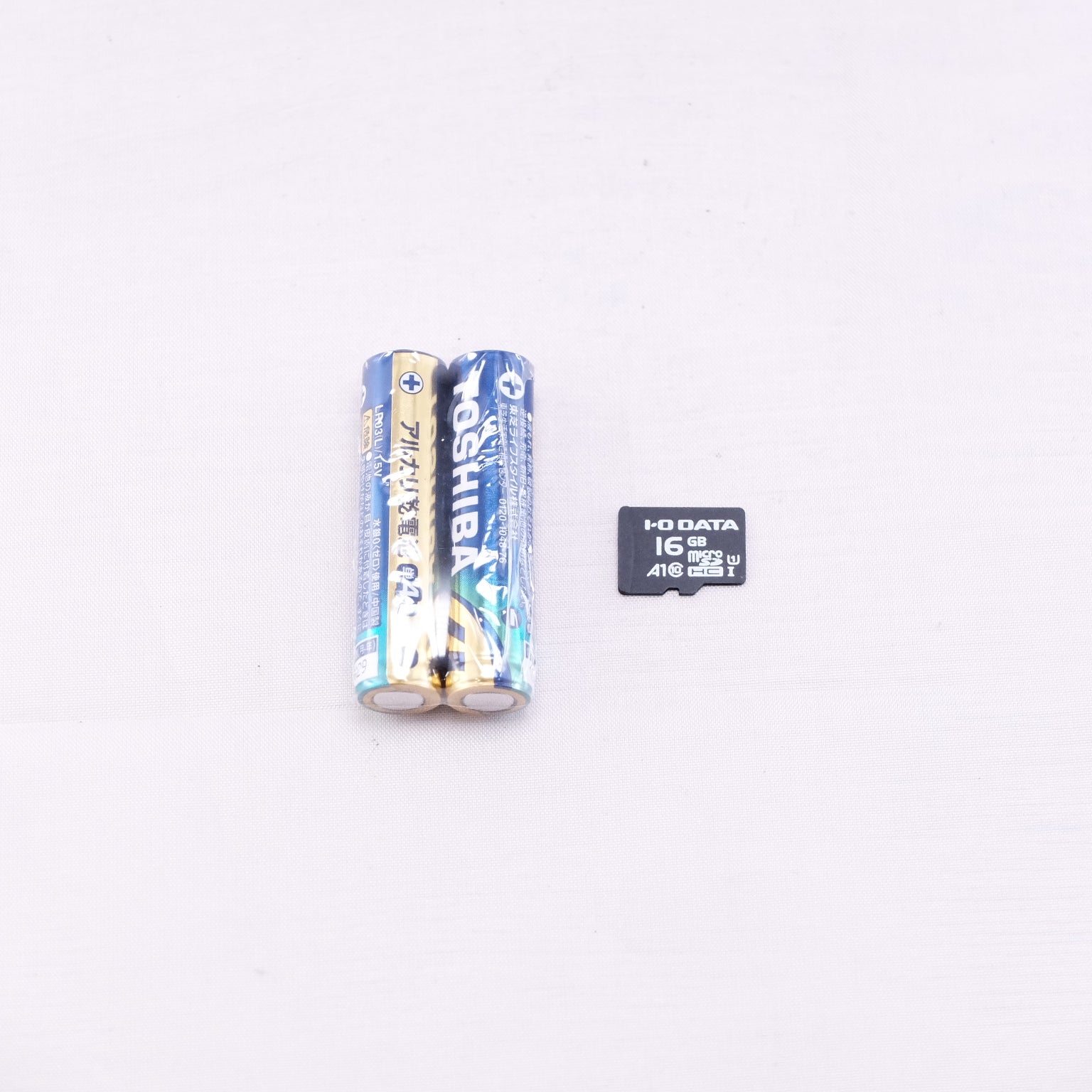 Two Toshiba batteries and a 16GB I-O DATA memory card on a light background.